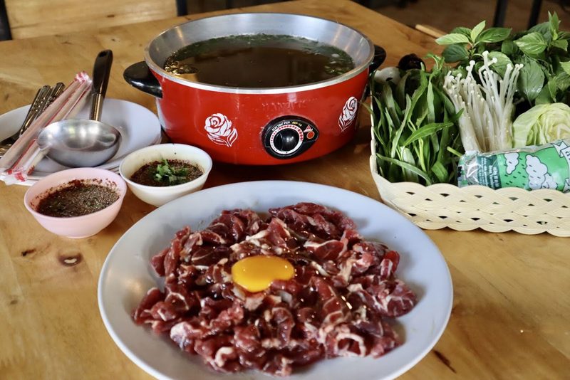 ชุดแจ่วฮ้อน หม้อสีแดงกับจานเนื้อสไลซ์วางไข่แดง ถ้วยแจ่ว และตะกร้าผักสด