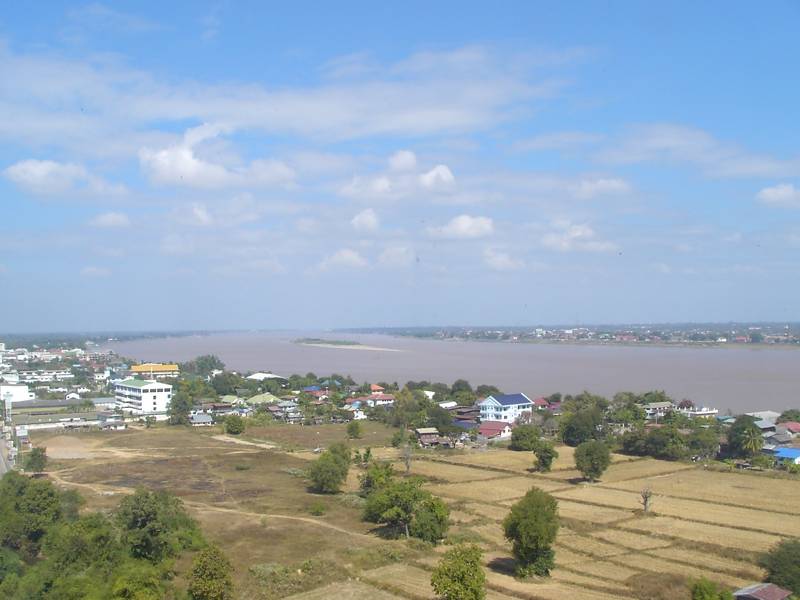 หลังคาบ้านเรือนและทุ่งนาในเมืองมุกดาหาร มีแม่น้ำโขงกว้างอยู่ด้านหลัง